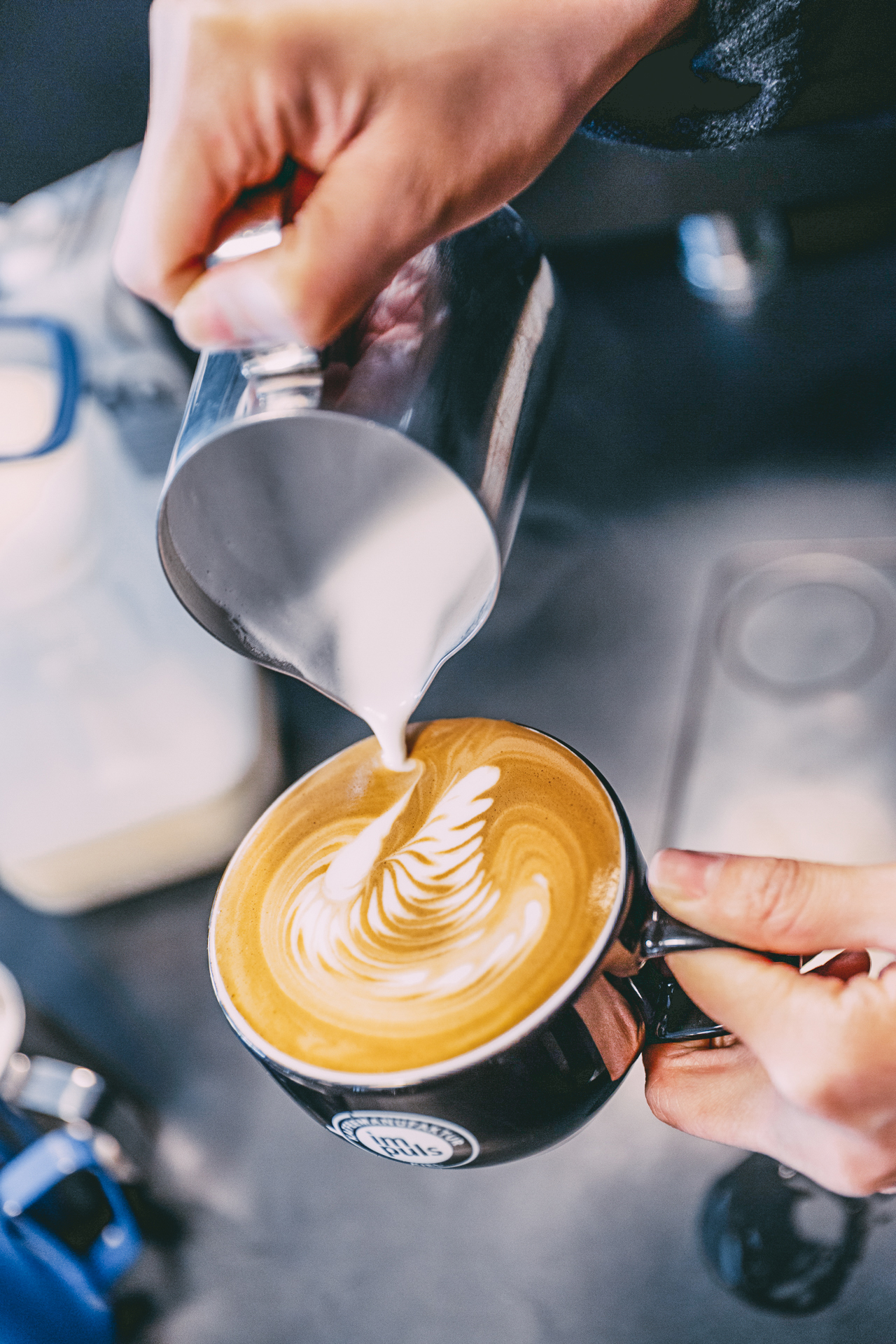 Milch wird in einen Kaffee gekippt und dabei Latte-Art praktiziert