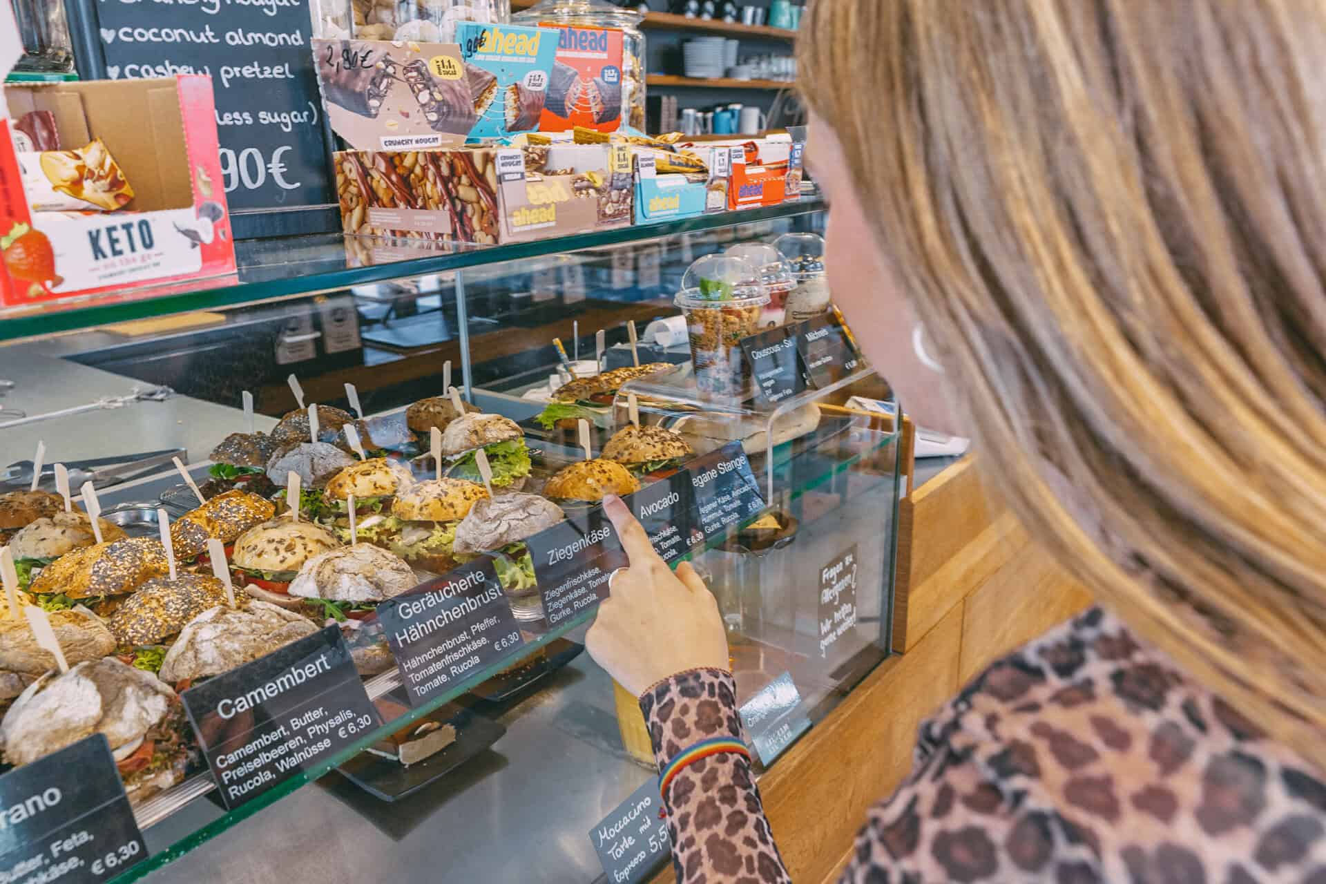 Finja steht vor der Vitrine mit belegten Brötchen und wählt es eines aus