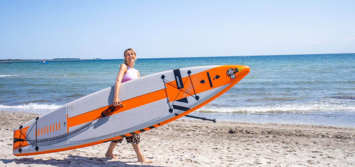 Finja mit einem einem SUP Board unterm Arm am Südstrand auf Fehmarn