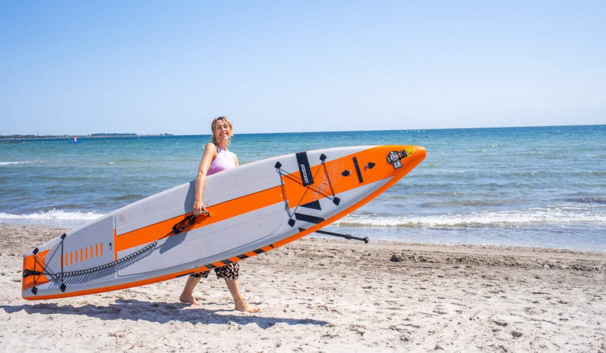 Finja mit einem einem SUP Board unterm Arm am Südstrand auf Fehmarn