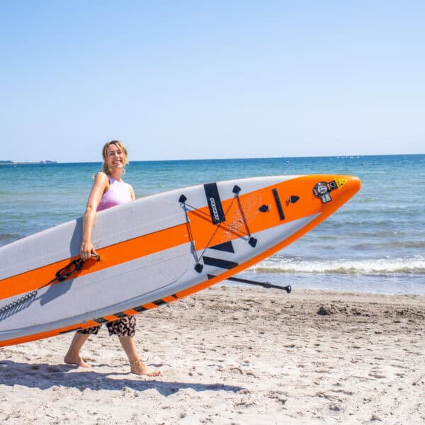 Finja mit einem einem SUP Board unterm Arm am Südstrand auf Fehmarn