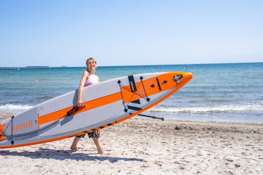 Finja mit einem einem SUP Board unterm Arm am Südstrand auf Fehmarn