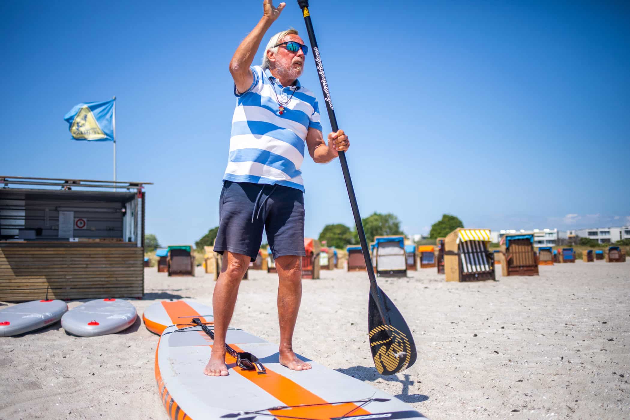 Ein Mitarbeiter von SUP Fehmarn steht an Land auf einem SUP Board mit einem Paddel in der Hand