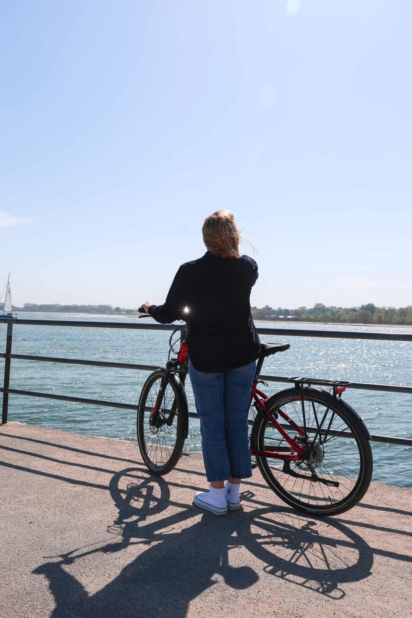 Maya hält ein Fahrrad und blickt auf das Meer