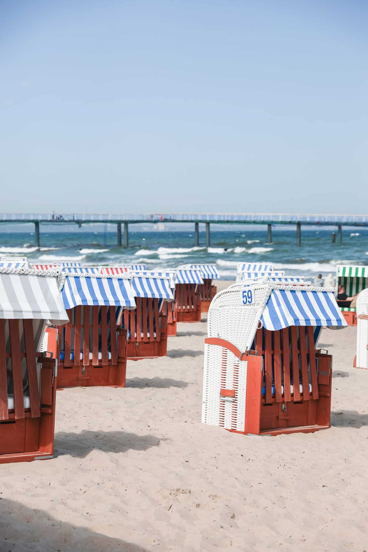 Blau-weiße, rot-weiße und grün-weiße Strandkörbe am Strand von Timmendorf, die Seebrücke im Hintergrund