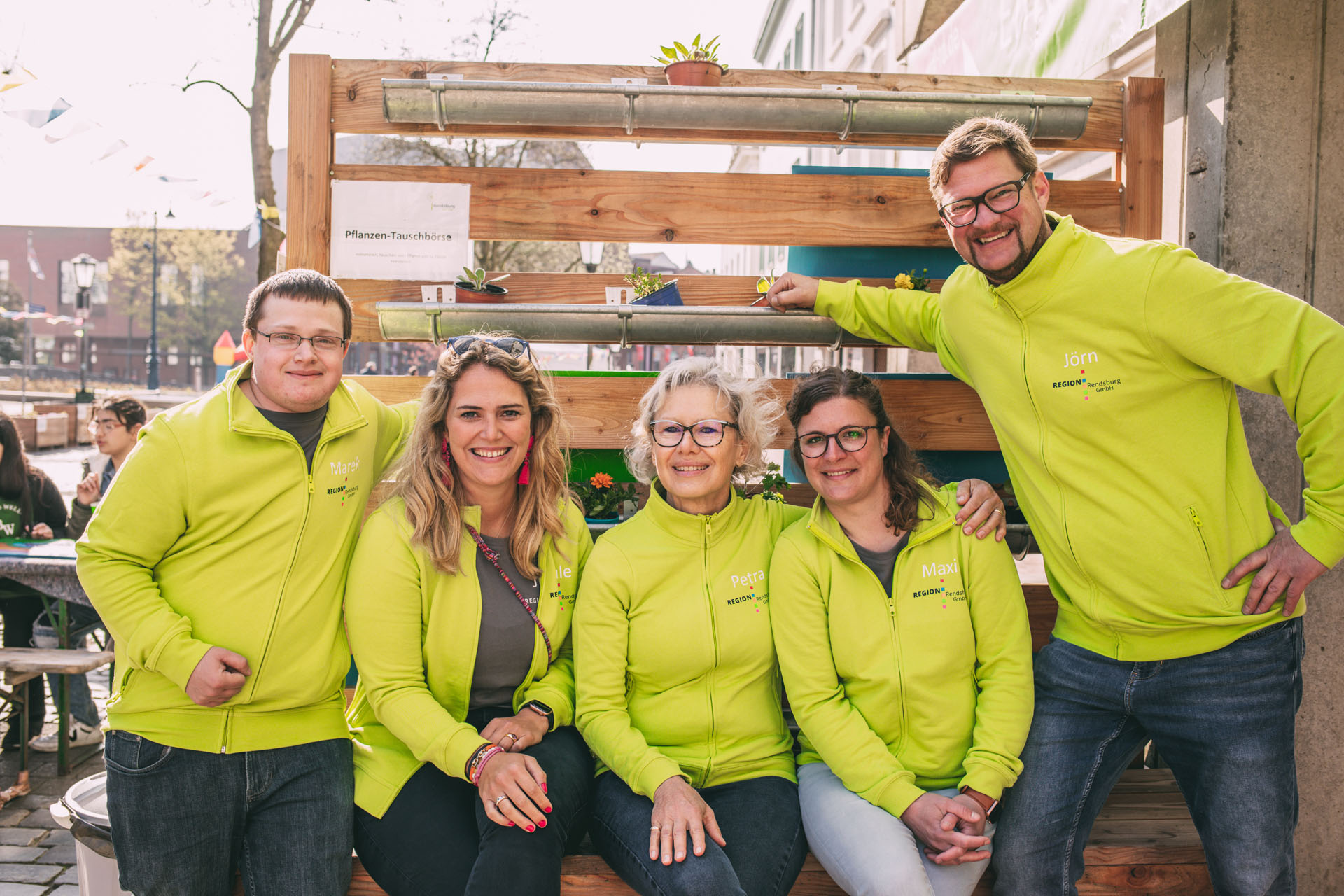 Das Team der Region Rendsburg GmbH sitzt auf einer Bank und schaut in die Kamera