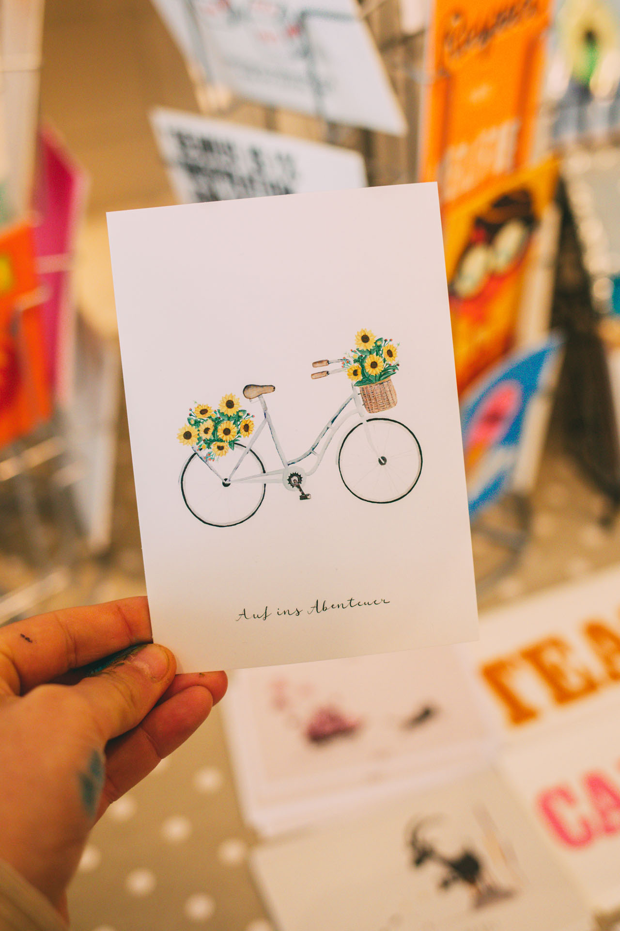 Zu sehen ist eine Postkarte mit einem gemalten Fahrrad und der Aufschrift: Auf ins Abenteuer