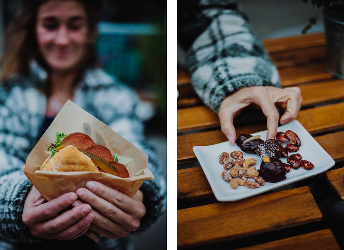 Mona hält ein veganes Sanwich mit veganer Salami und nimmt sich vegane Süßigkeiten von einem Teller