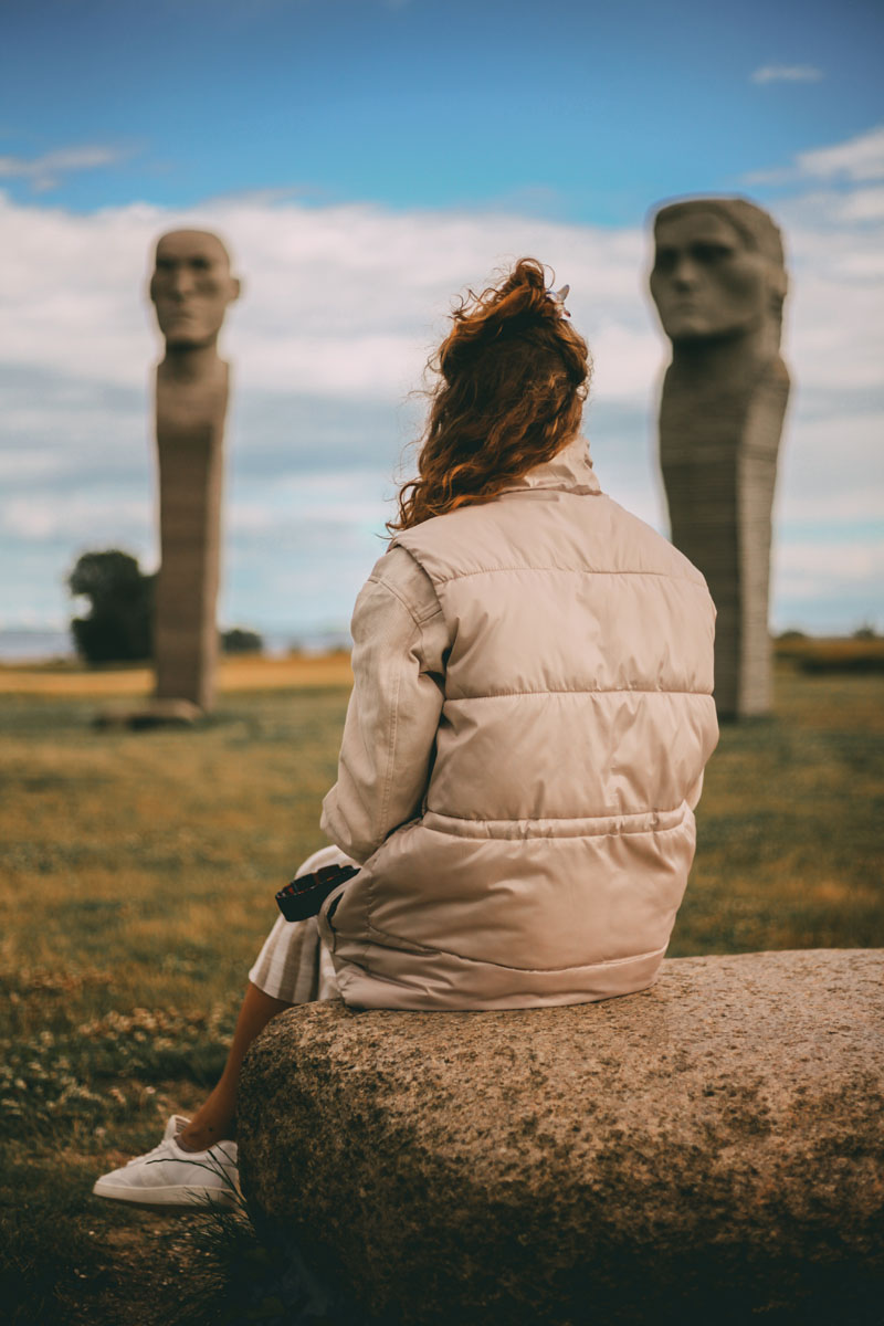 Mona sitzt auf einem Stein und schaut auf die Steinfiguren der Dodekalitten auf Lolland