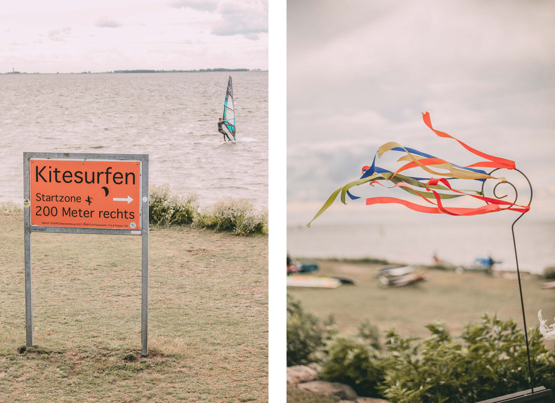 Ein Schild mit der Aufschrift "Windsurfen", ein Windsurfer im Hintergrund auf dem Wasser und ein Windspiel