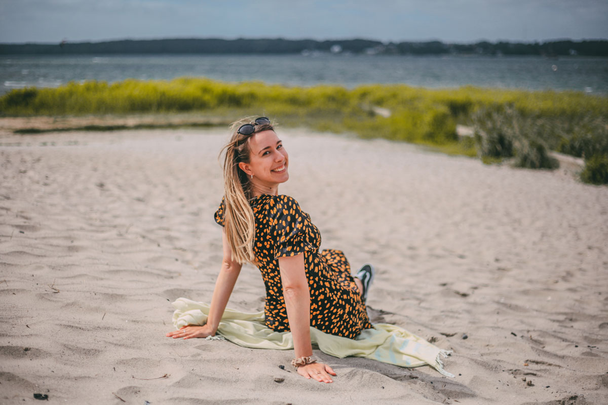 Finja sitzt im Sand am Strand Solitüde in Flensburg