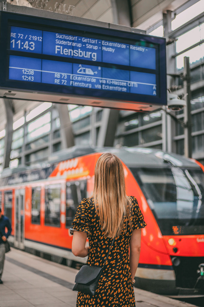 Finja steht am Gleis vor einem Zug und schaut auf die Zuganzeige