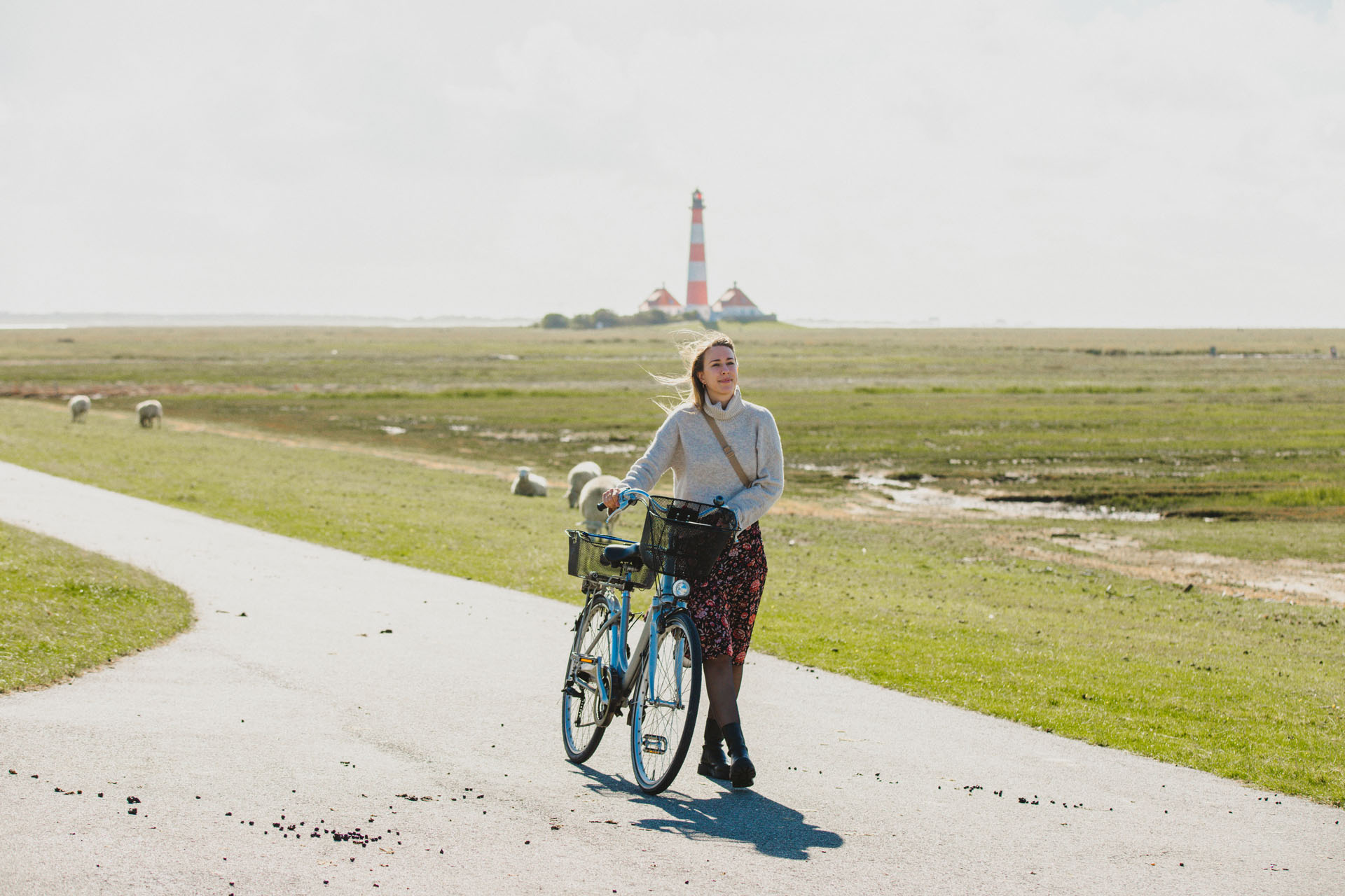 Finja schiebt ein Fahrrad am Deich vor dem Leuchtturm Westerheversand