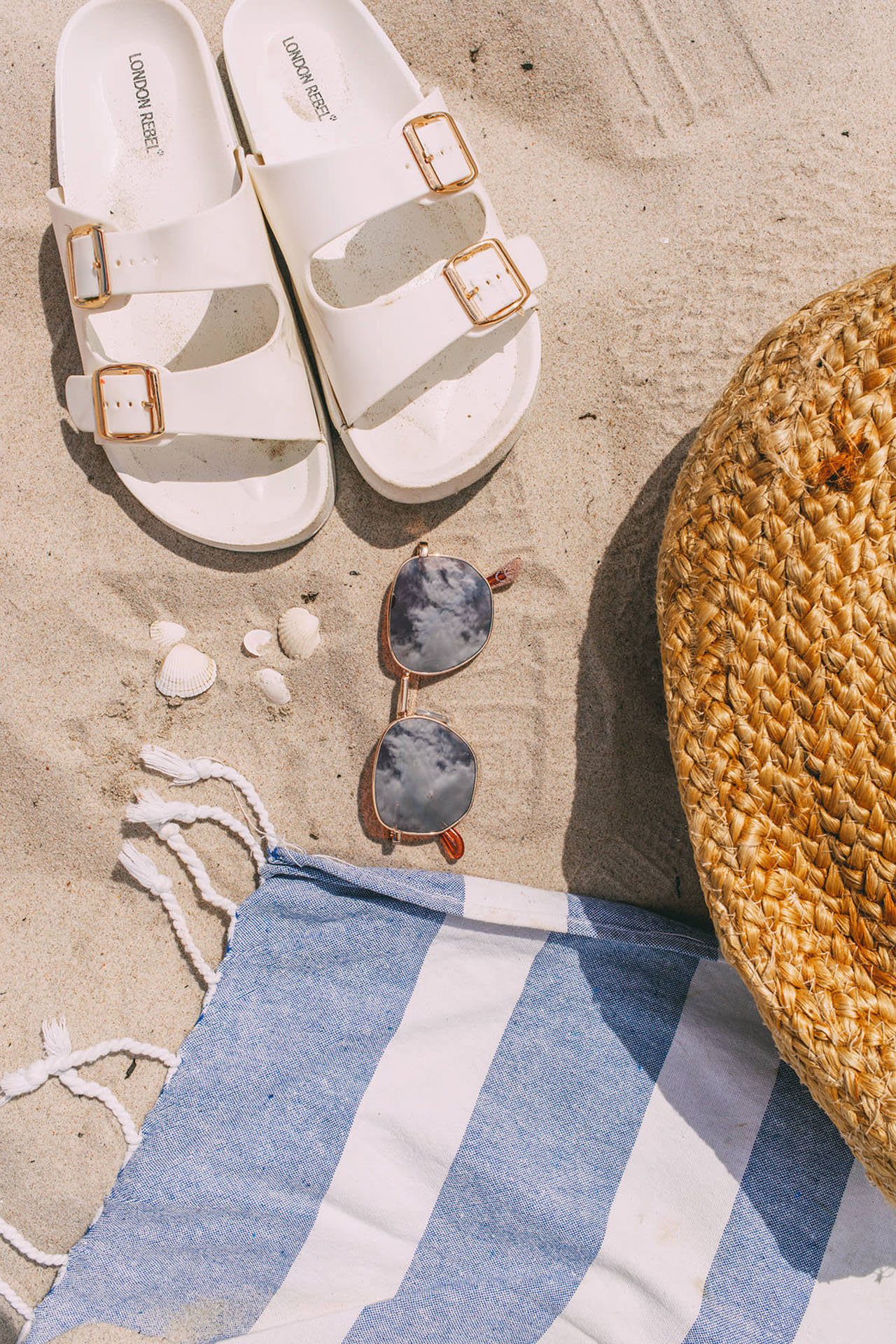 Sandalen, Sonnenbrille und Badetuch im Sand