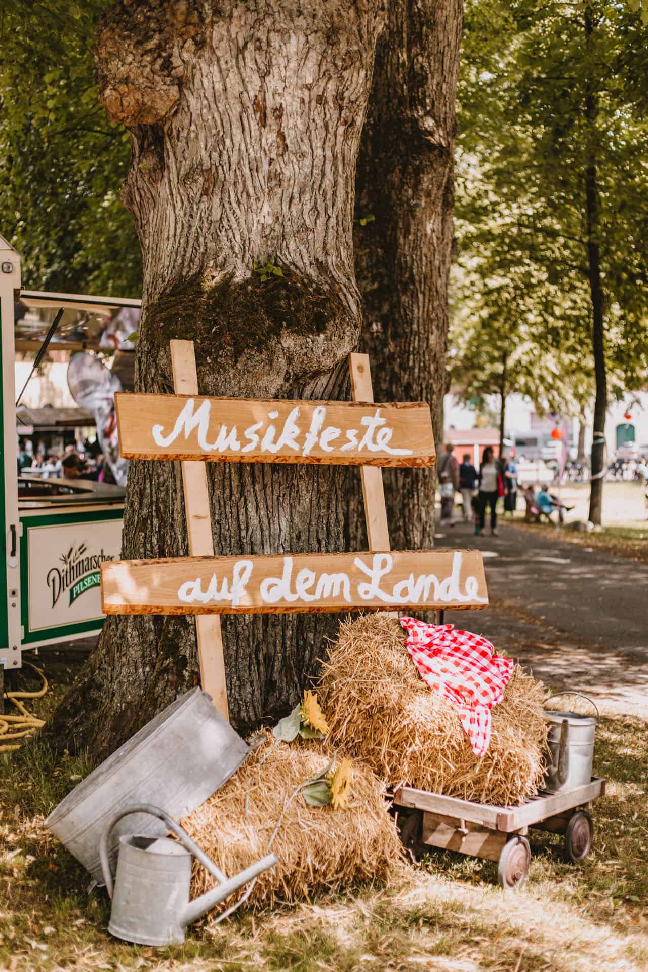 Ein Holzschild mit der Aufschrift „Musikfeste auf dem Lande“ lehnt an einem Baum