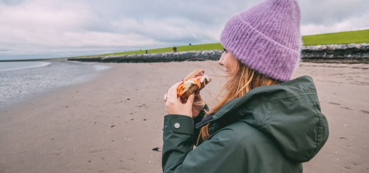 Maya steht am Strand an der Nordsee und isst ein Fischbrötchen