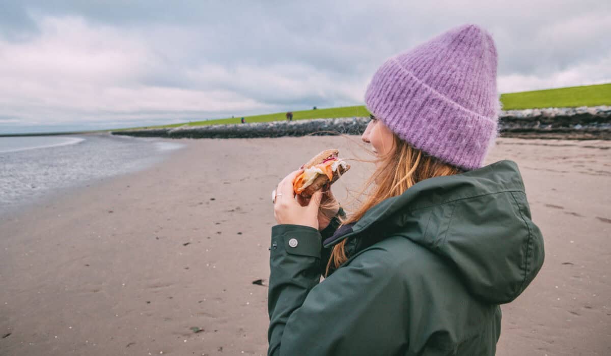 Maya steht am Strand an der Nordsee und isst ein Fischbrötchen