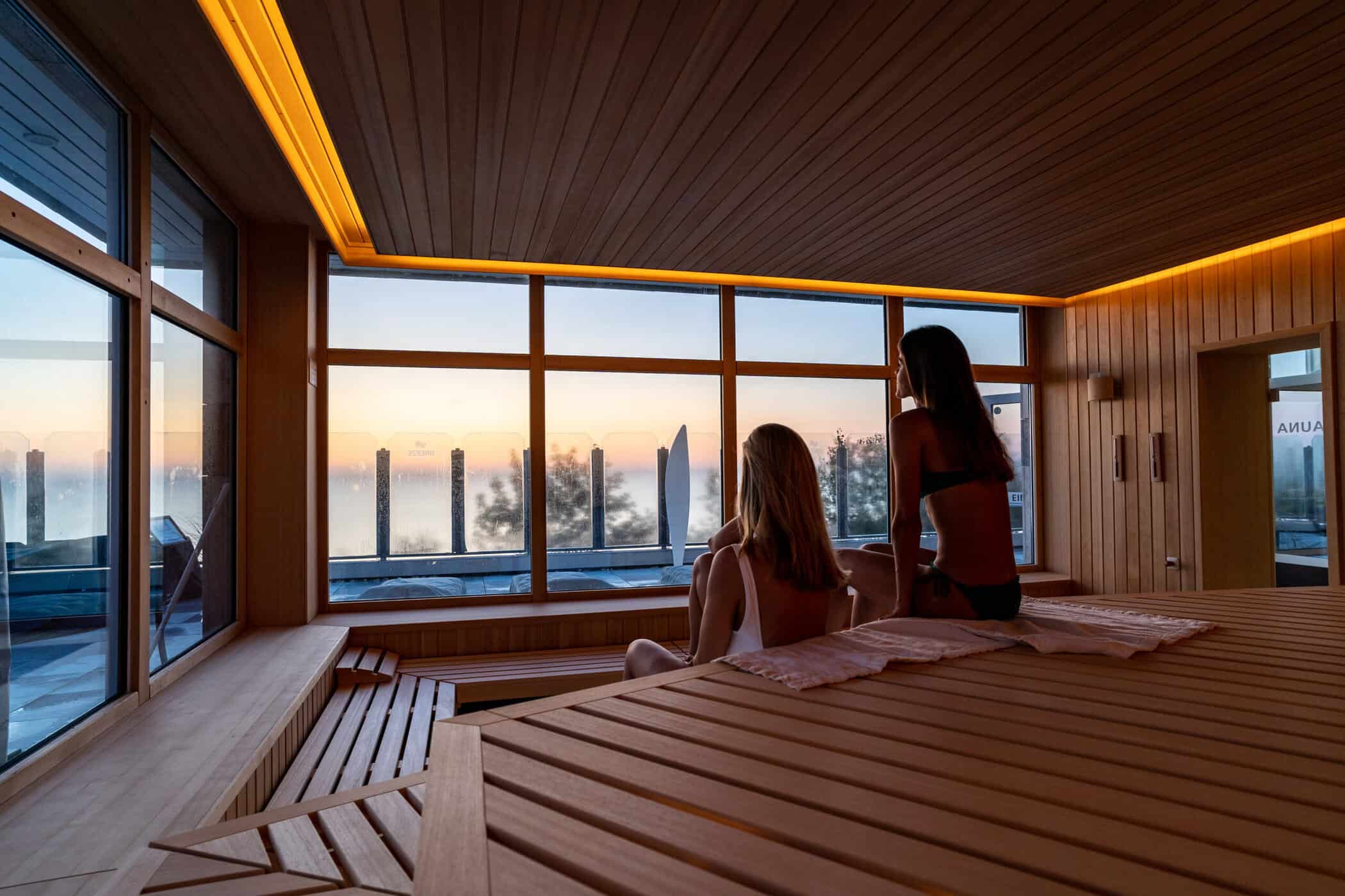 Zwei Frauen sitzen in der Sauna und blicken aus dem Fenster auf die Ostsee