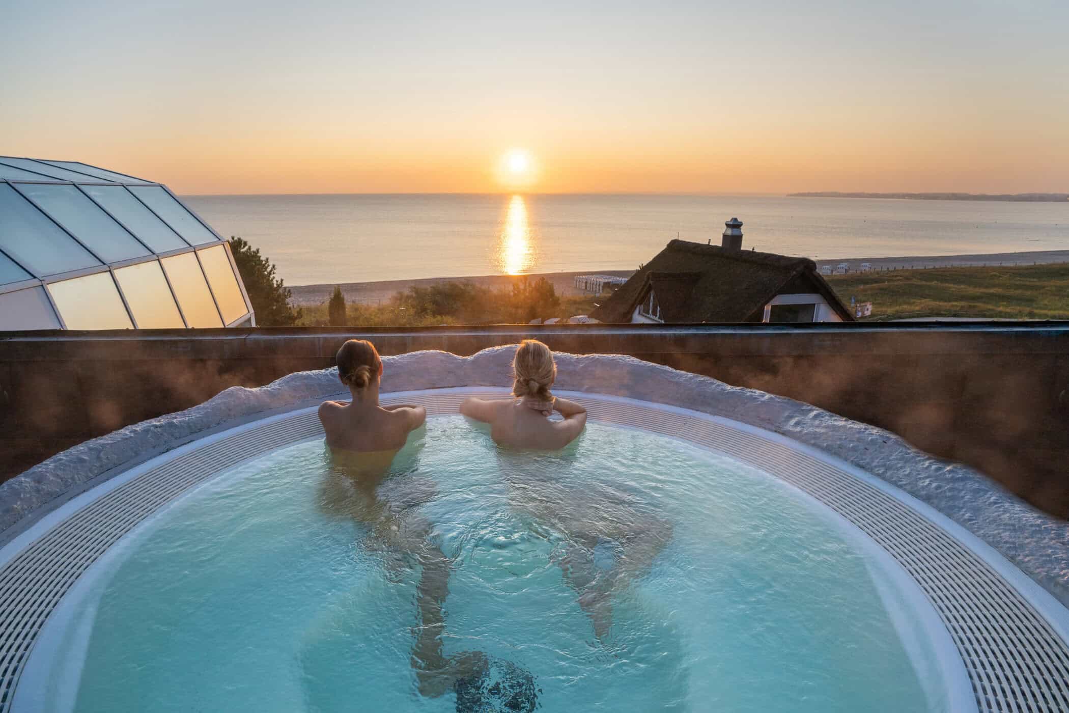 Zwei Fragen sitzen im Outdoor-Whirlpool und blicken auf die untergehende Sonne über der Ostsee