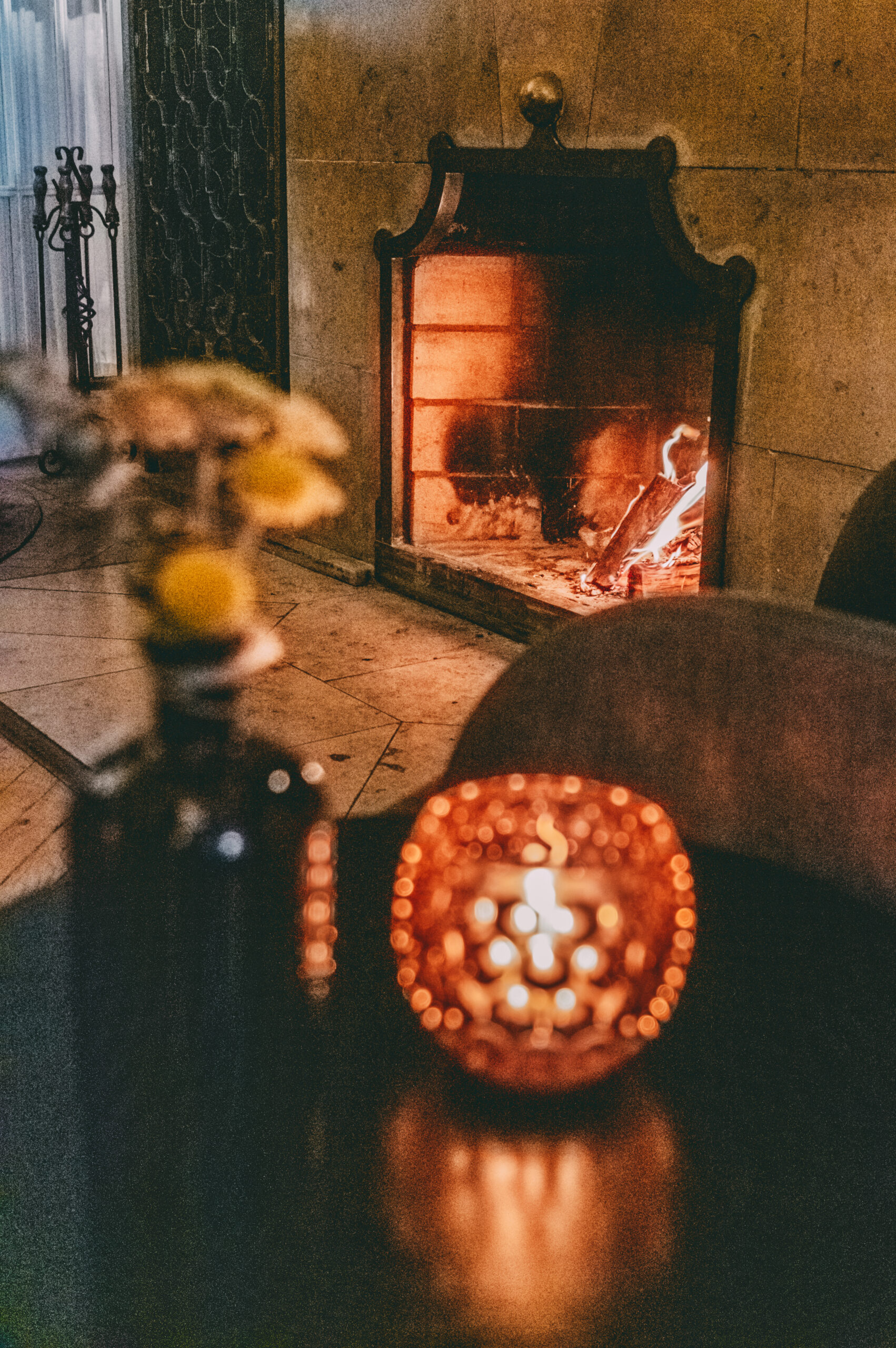 Ein Trockenblumenstrauß und ein Teelicht, im Hintergrund an brennendes Kaminfeuer