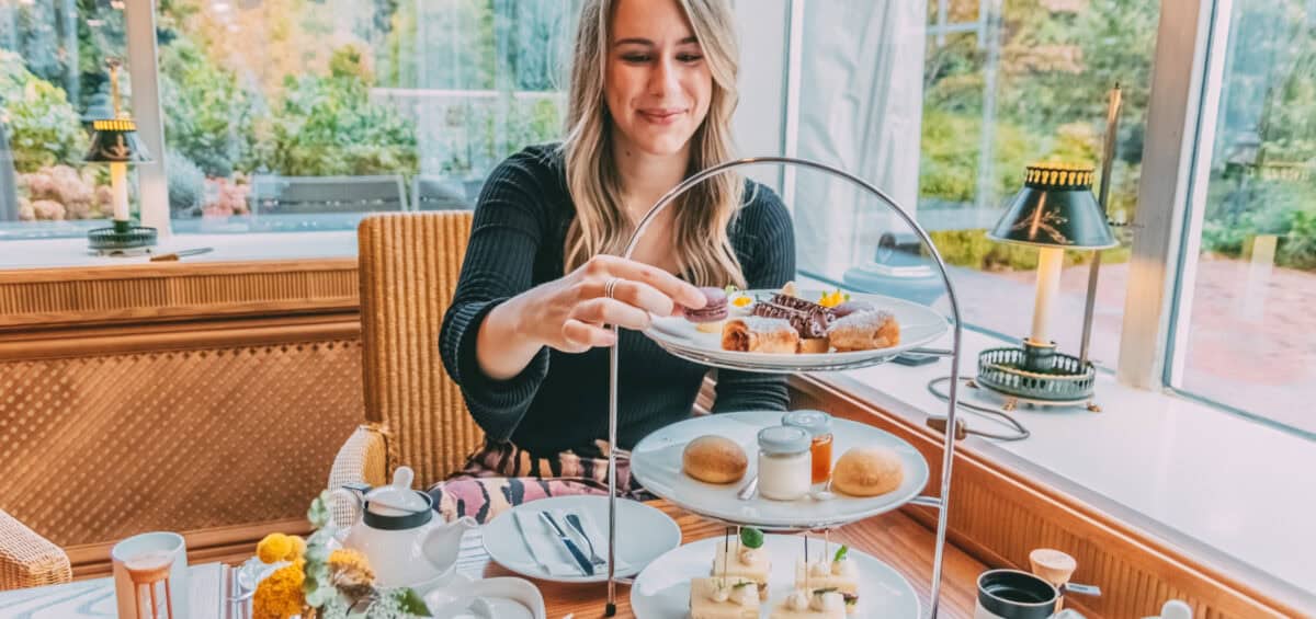 Finja sitzt am gedeckten Tea-Time-Tisch und greift nach Gebäck auf einer Etagere