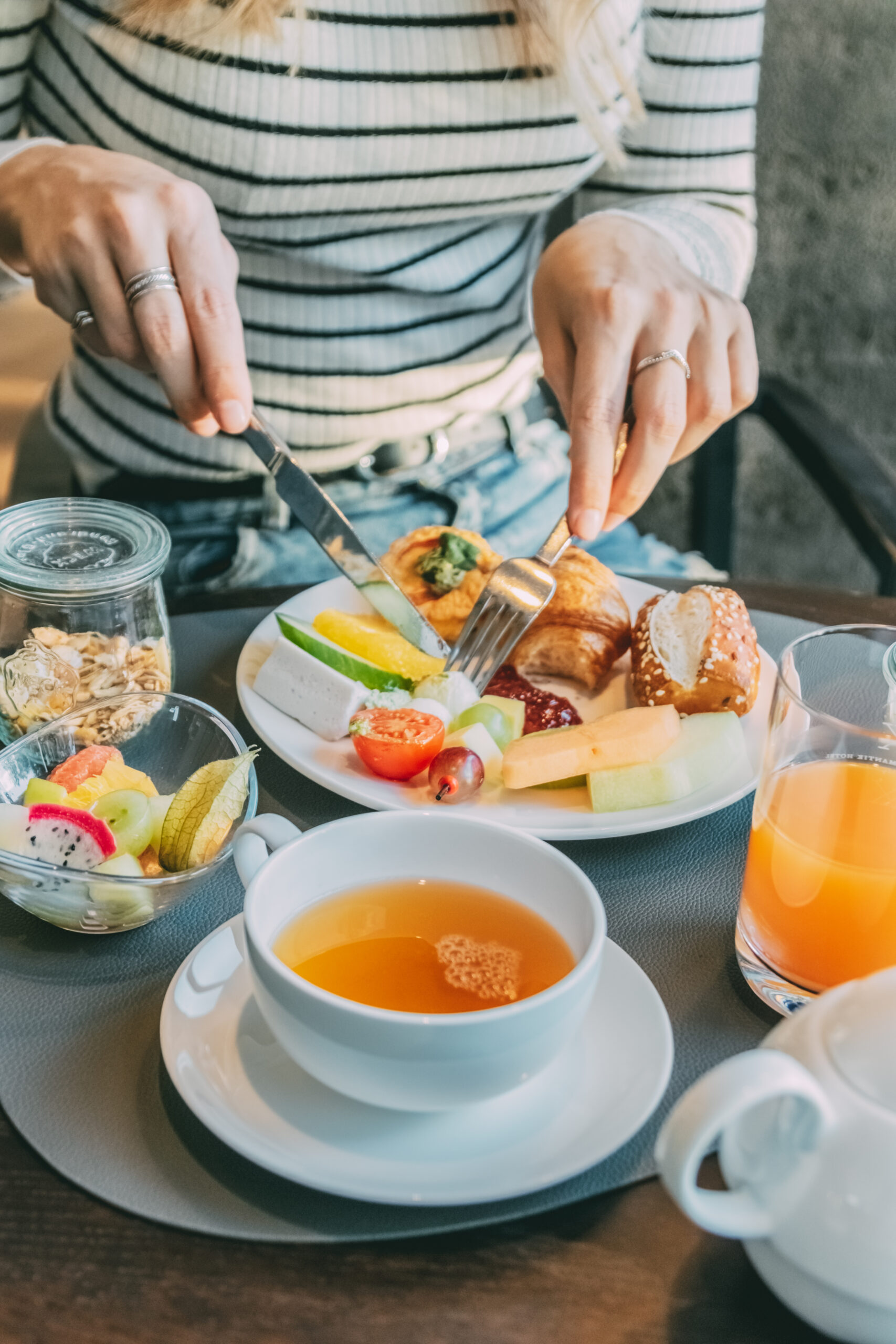 Voller Frühstücksteller, daneben eine Tasse Tee, ein Glas Saft, eine Schüssel Obst und ein Weckglas mit Müsli