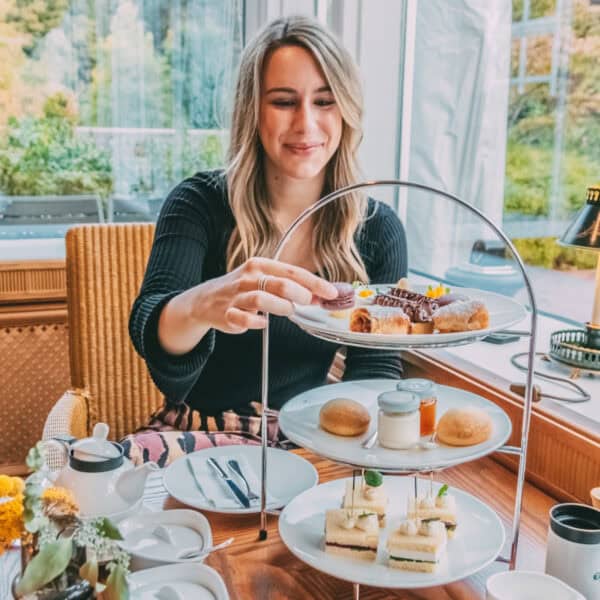 Finja sitzt am gedeckten Tea-Time-Tisch und greift nach Gebäck auf einer Etagere