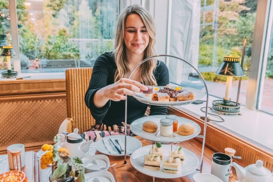 Finja sitzt am gedeckten Tea-Time-Tisch und greift nach Gebäck auf einer Etagere