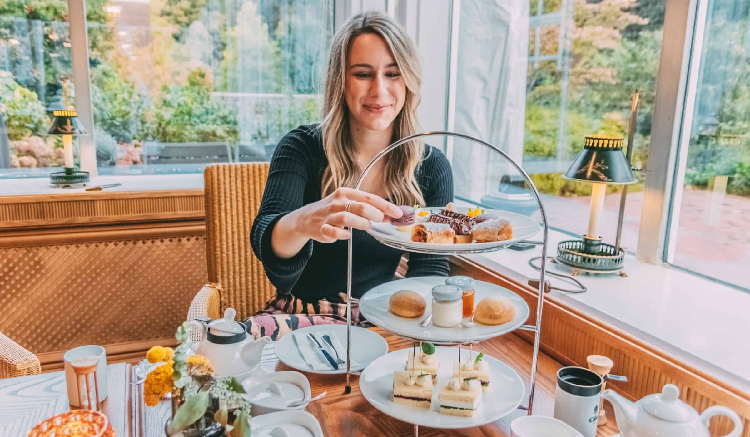 Finja sitzt am gedeckten Tea-Time-Tisch und greift nach Gebäck auf einer Etagere