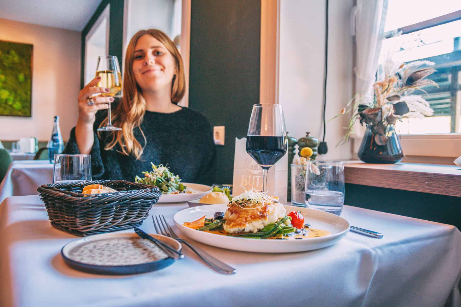 Finja sitzt am Esstisch im Restaurant BUTZ und hält ein Weinglas in die Luft