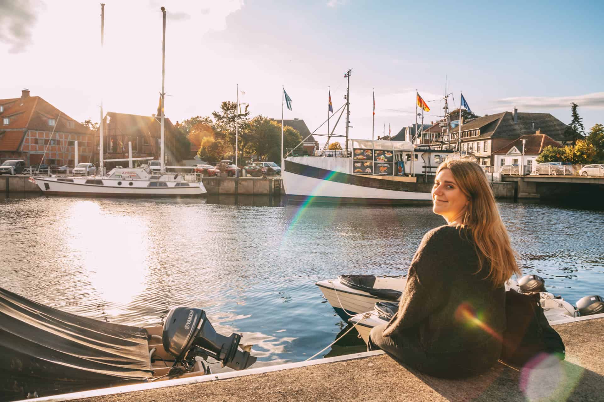 Maya sitzt am Hafen in Neustadt in Holstein bei strahlendem Sonnenschein