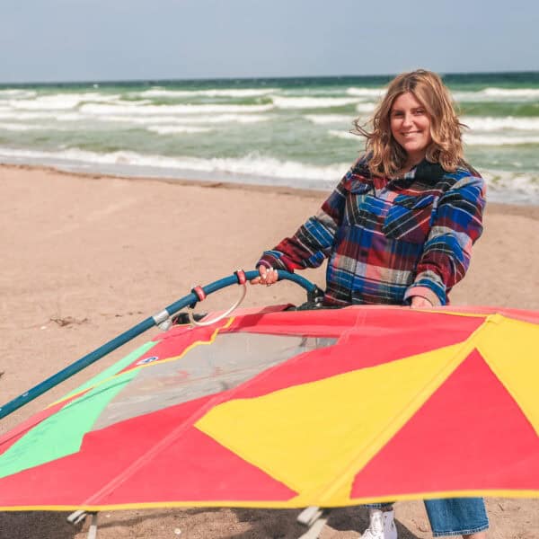 Maya steht am Strand und hält ein Surfsegel