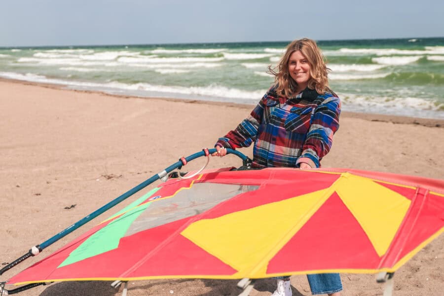 Maya steht am Strand und hält ein Surfsegel