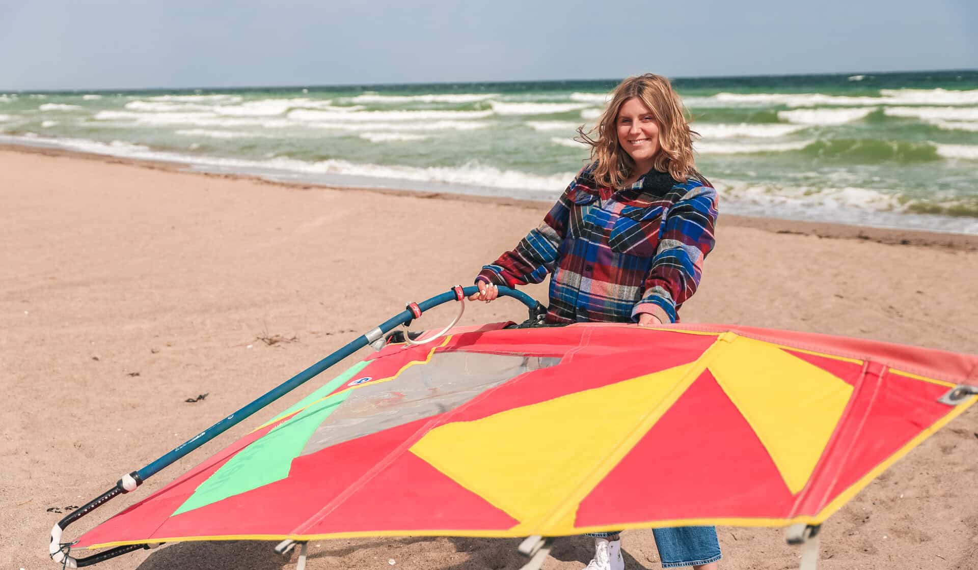 Maya steht am Strand und hält ein Surfsegel