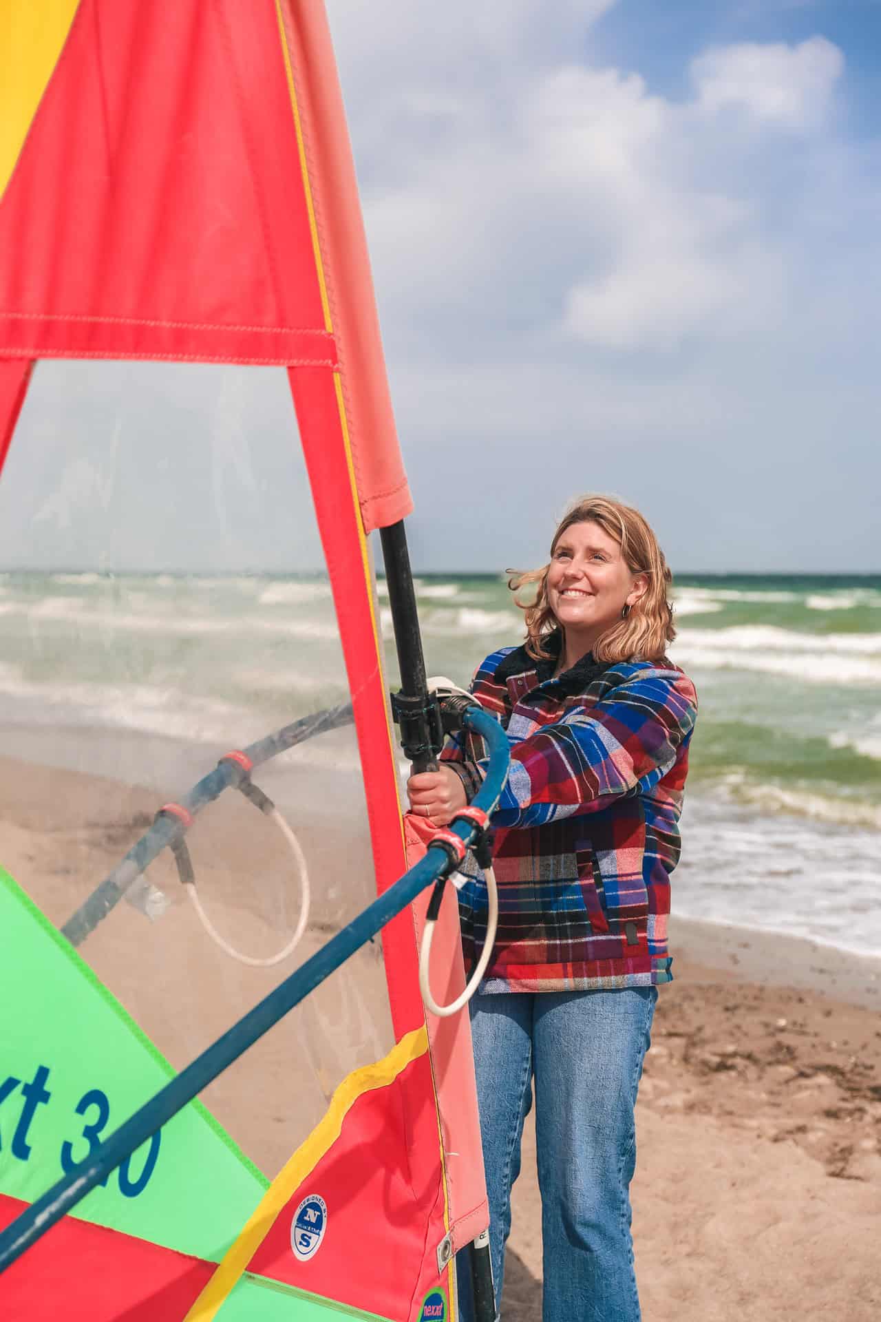 Maya steht am Strand von Dahme vorm Meer und hält ein Surfsegel