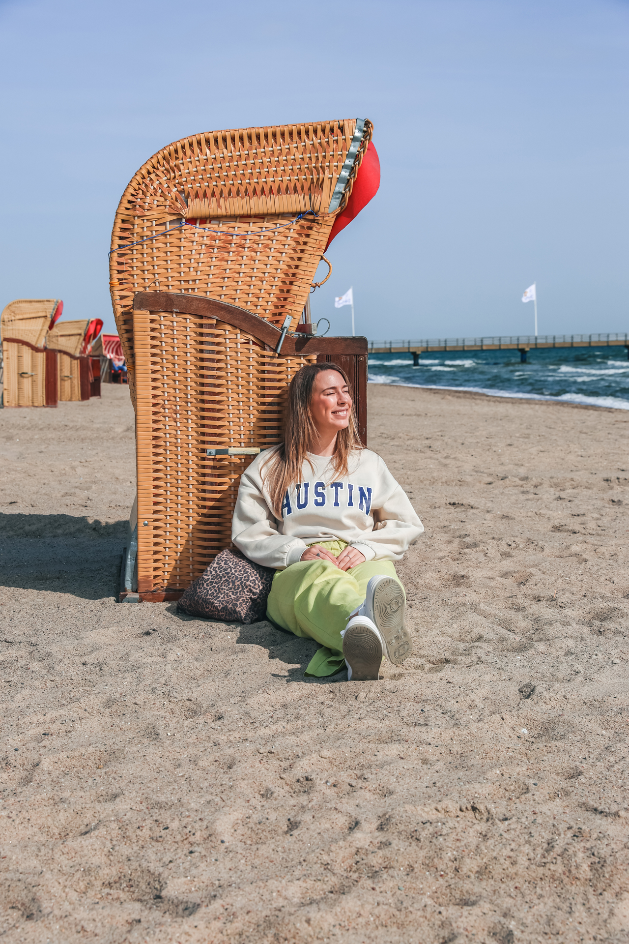 Finja sitzt am Strand von Dahme im Sand und lehnt sich an einen Strandkorb
