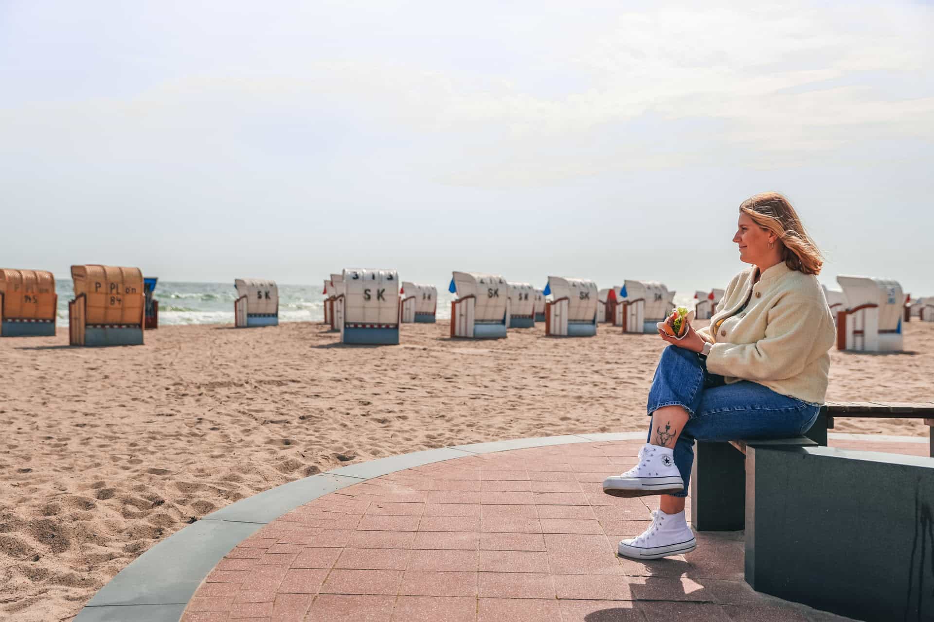 Maya sitzt am Strand von Dahme und hält ein Fischbrötchen