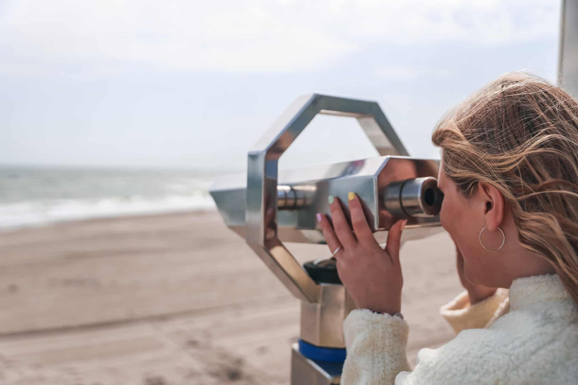 Maya schaut durch ein Fernglas aufs Meer am Strand von Dahme